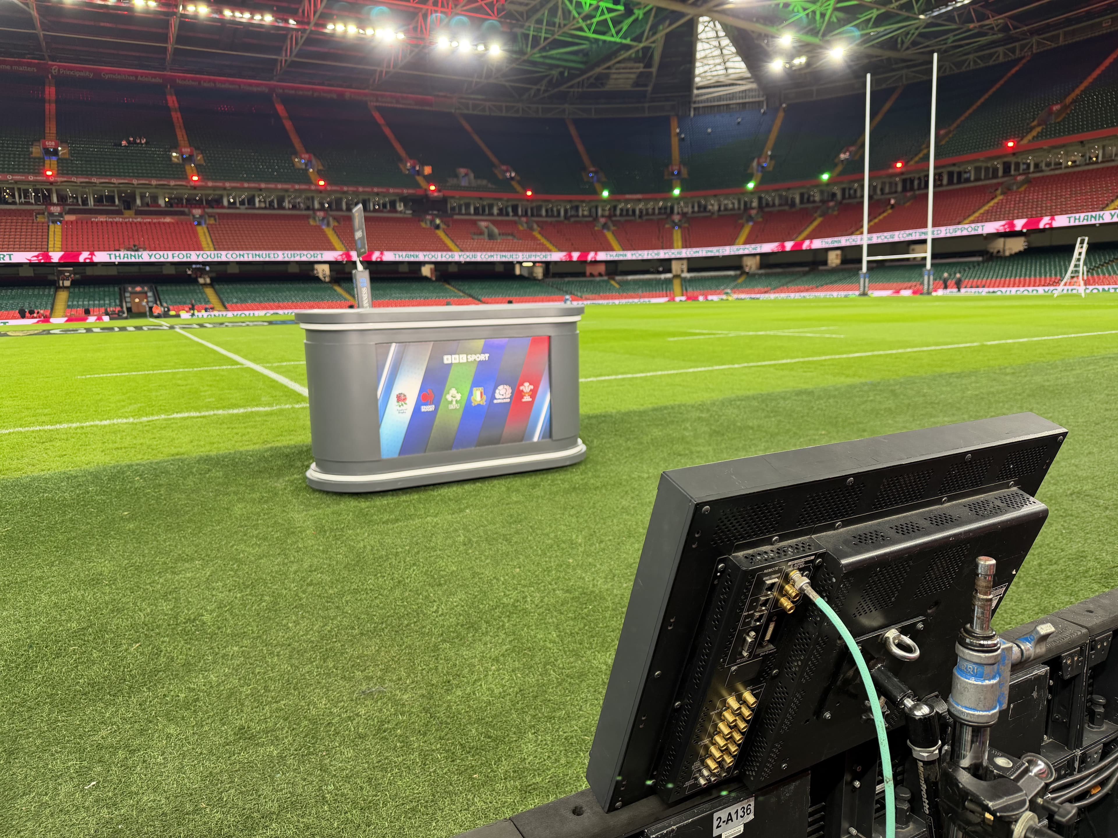 BBC Sport desk and monitor on a rugby pitch inside a large, empty stadium.